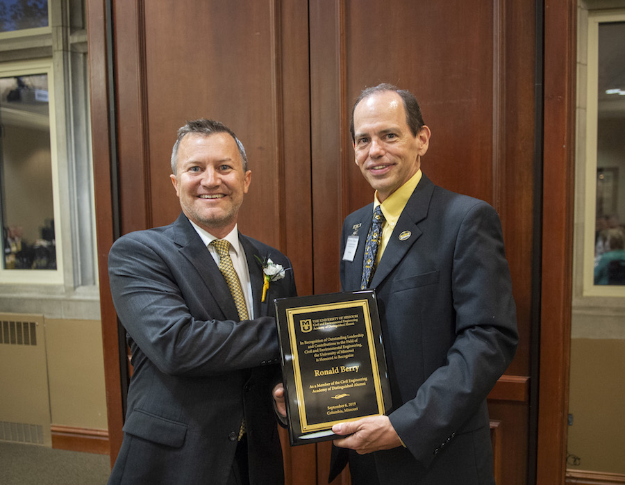 Two men in suits hold a plaque.