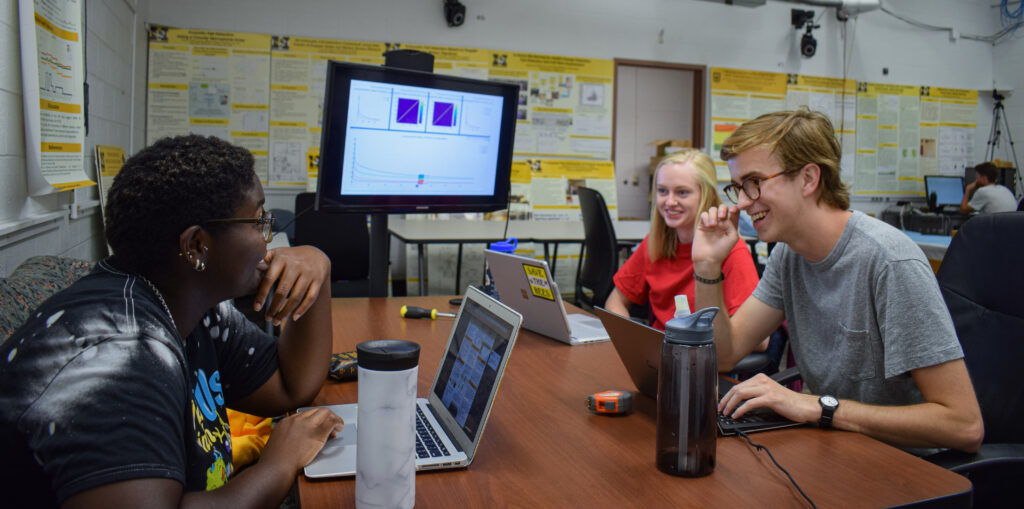 Three students share a laugh while working on laptops.