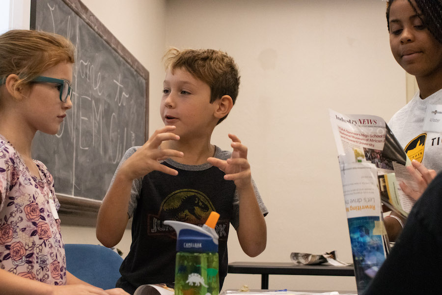 A boy and a girl collaborate on a project while a counselor looks on.