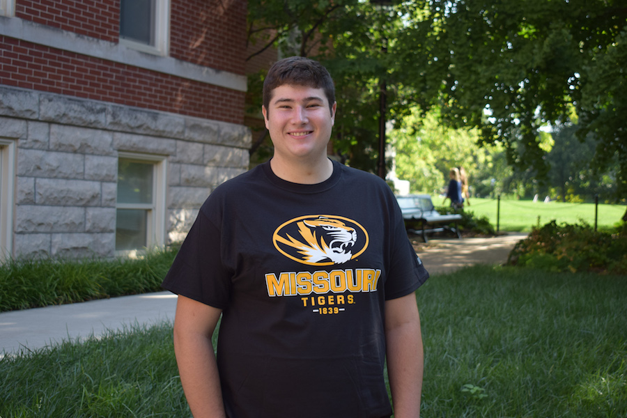 A young man in a Mizzou shirt stands in a courtyard.