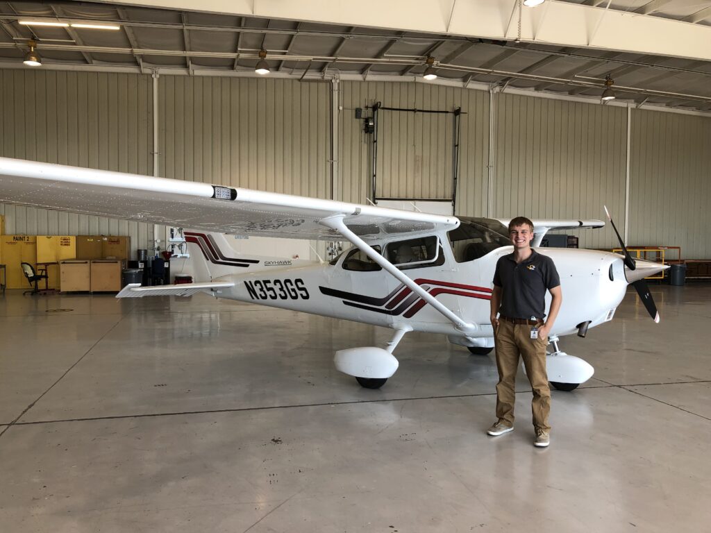 A man in a polo stands in front of a plane.