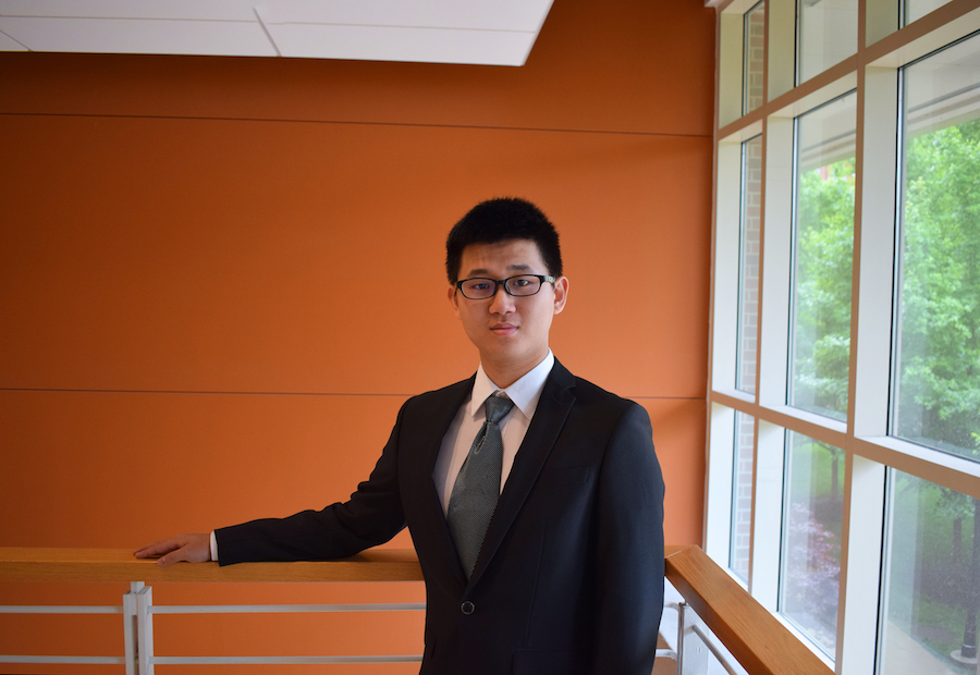 A man in glasses and a suit poses on a balcony.