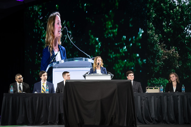 A woman presents in front of a large screen.