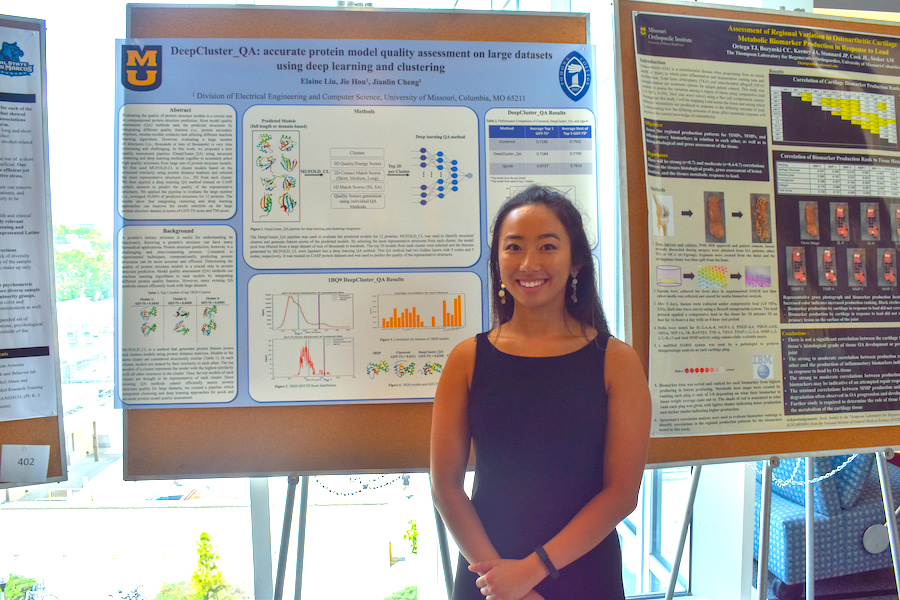 A young woman stands in front of a poster.