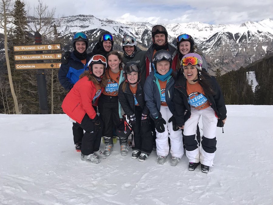 Students in snow gear standing on a snowy ridge.