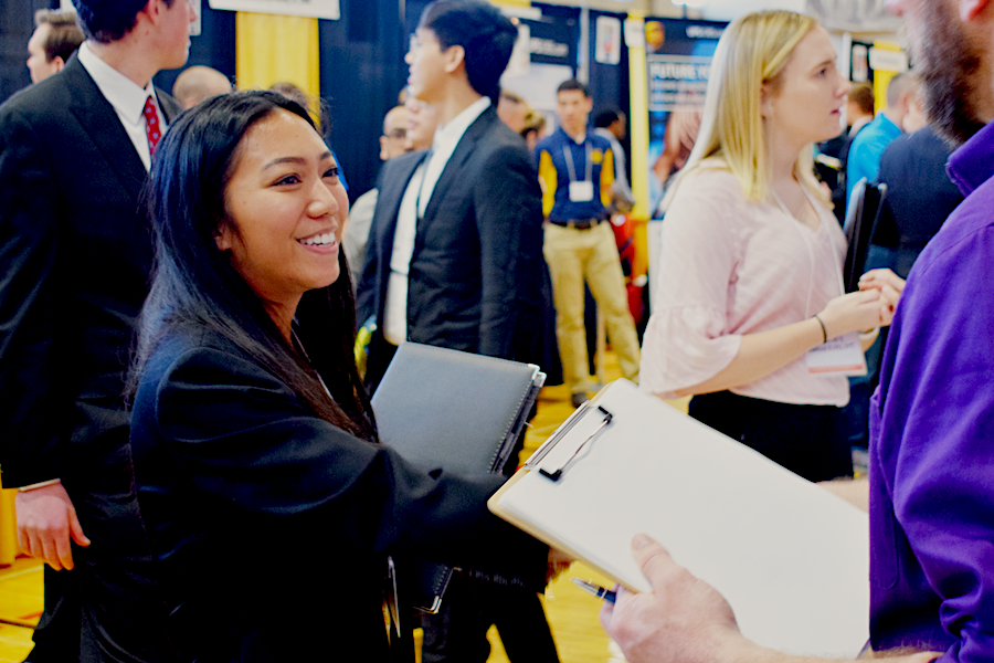 Celestene Sebag shakes hands with an employer holding a clipboard at the career fair.