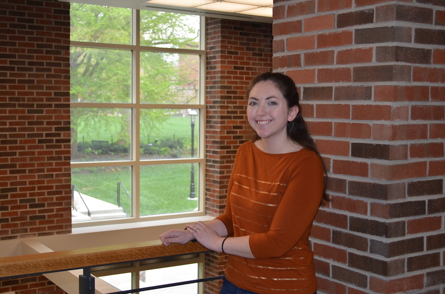 A woman in orange stands by a balcony.