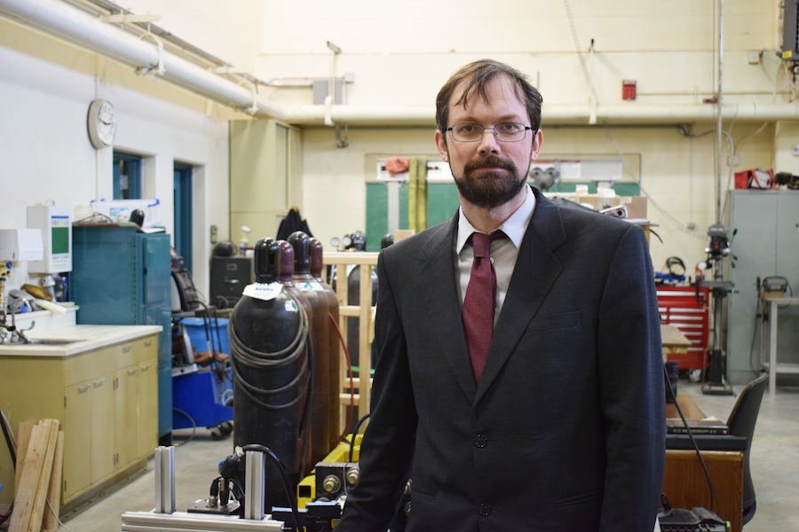 A man in glasses, jacket and tie stands in a workshop.