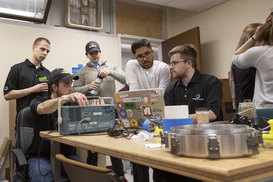 Students crowd around a laptop.